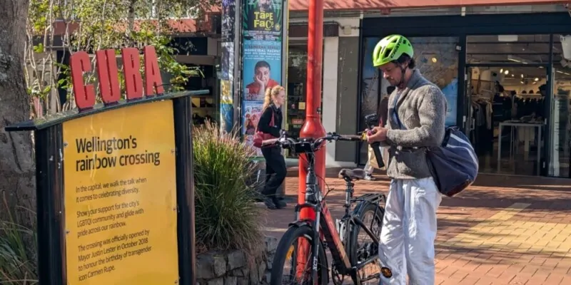 Un cycliste au casque vert gare son vélo sous le panneau de Cuba Street à Wellington Scène de rue vivante et décontractée dans l’un des quartiers les plus emblématiques de la ville