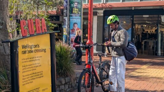 Un cycliste au casque vert gare son vélo sous le panneau de Cuba Street à Wellington Scène de rue vivante et décontractée dans l’un des quartiers les plus emblématiques de la ville